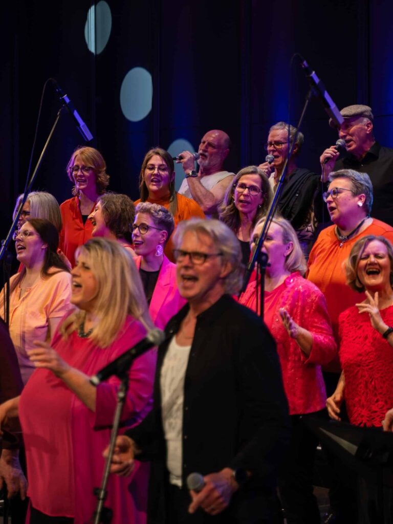 Einige Menschen, bunt gekleidet, singen dynamisch vor Mikrofonen