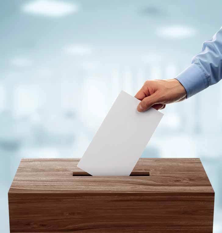 Das Foto zeigt eine Hand die einen Stimmzettel in eine Wahlurne einwirft.