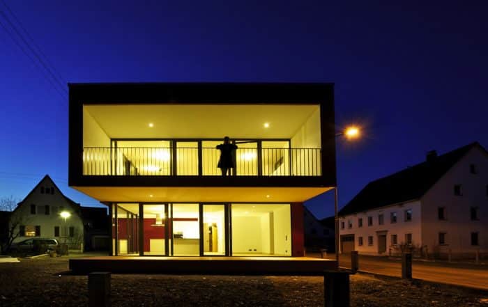 Hell beleuchtetes Haus mit moderner Architektur und einer auf dem Balkon stehenden Person