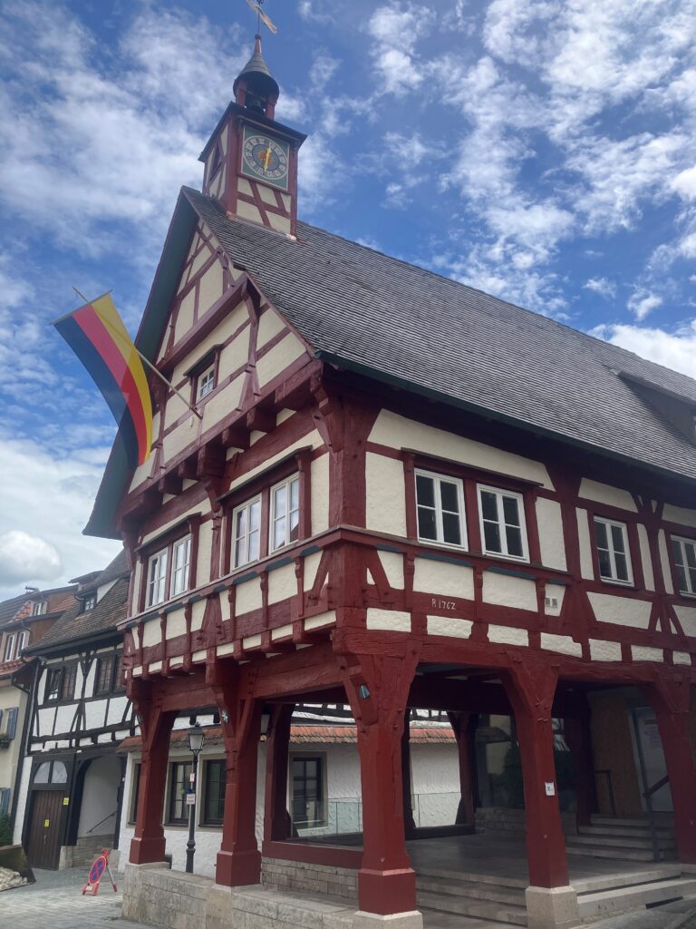 Das Rathaus von Mühlheim, ein ochsenblutroter Fachwerkbau, vor blauen Himmel mit kleinen Wölkchen, am Rathaus ist die schwarz-rot-goldene Deutschlandflagge aufgehängt